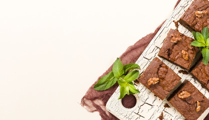 Brownie sweet chocolate dessert with walnuts and meant leaves on retro board with copy space on pastel beige background.