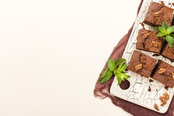 Brownie sweet chocolate dessert with walnuts and meant leaves on retro board with copy space on pastel beige background.