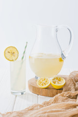 close up view of lemonade in glass with straw and jug on white wooden surface on grey backdrop