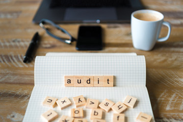 Closeup on notebook over wood table background, focus on wooden blocks with letters making Audit word