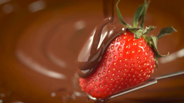 Strawberry in chocolate. Melted chocolate pouring on fresh ripe juicy strawberry closeup over swirl brown background. Fondue. Dessert. Slow motion 4K UHD video 3840X2160