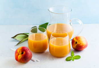 peach juice in glasses and a decanter and fresh peaches with leaves on a table. blue background. copy space