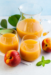peach juice in glasses and a decanter and fresh peaches with leaves on a table. blue background. copy space