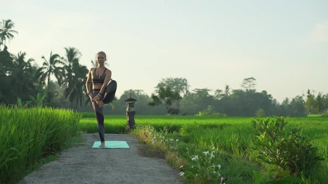 Fit girl do yoga extended hand to big toe pose at rice field rapid slow motion
