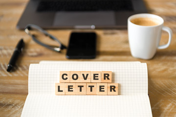 Closeup on notebook over wood table background, focus on wooden blocks with letters making COVER...