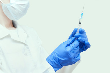 A nurse in blue gloves with a syringe in her hands on a white background. Close-up