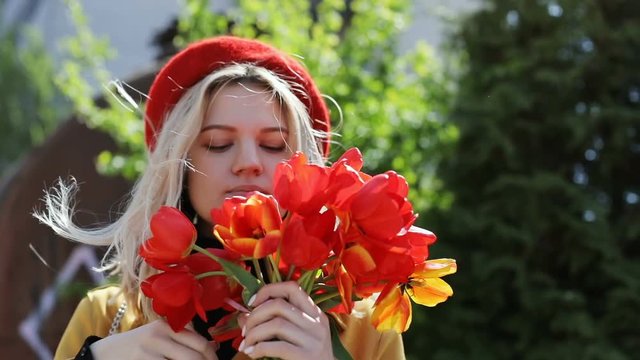 blonde gorgeous woman holding bunch of red tulips outside in sunny windy day urban spring fashion clothes beauty freshness cool advertisement of modern flower delivery company enjoy flowers aroma