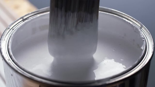 Hand of painter dipping a brush into a bucket with white paint
