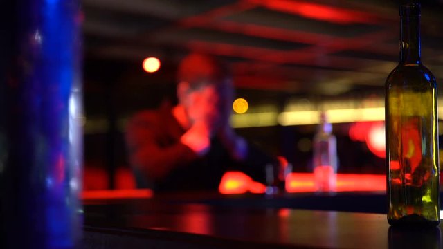 Depressed man drinking whiskey alone in nightclub, thinking over problems