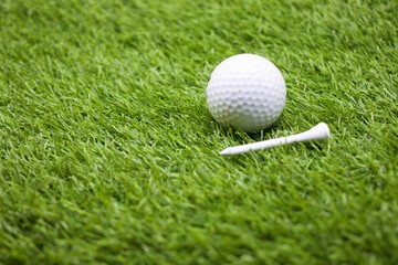 Golf ball and tee are on green grass