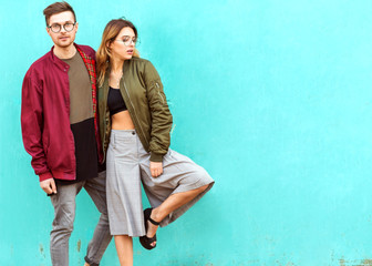 fashion couple in their glasses with burgundy clothes posing on a blue wall