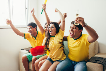 Group of friends watching soccer game on television, celebrating goal and screaming
