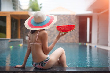 water melon in hand of woman sitting at edge of swimming pool, enjoy and relax happiness emotion for life comfortable in diet fruit with exercise