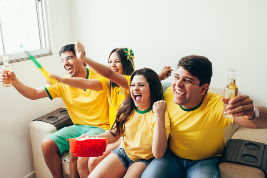 Group of friends watching soccer game on television, celebrating goal and screaming