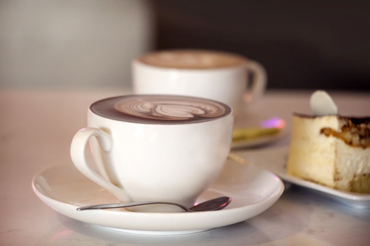 Two cappuccino cups with cheese cake on the table in cafe. Cafe background.
