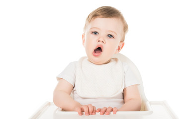 yawning baby boy in bib sitting in highchair isolated on white background