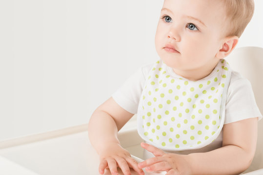 portrait of baby boy in bib sitting in highchair isolated on white background