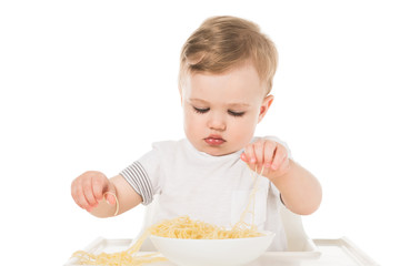 adorable child eating spaghetti by hands and sitting in highchair isolated on white background