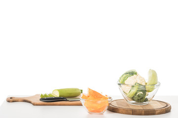 closeup view of cutting boards, knife, bowls, zucchinis, pumpkin and cauliflower on table isolated on white background