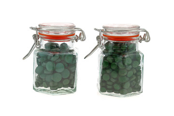 Algae spirulina tablets. pills of spirulina in two transparent glass jars isolated on white background.Super food concept. seaweed in tablets.nature. Food supplements 