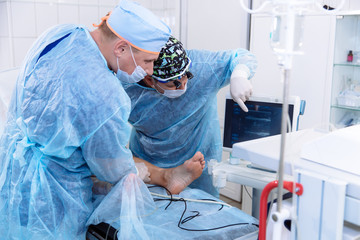 A team of doctors in the operating room conducts medical procedures. Surgeons in sterile clothing work in the hospital. Medical equipment in the clinic.
