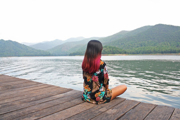 Happy asian woman sitting on the edge of a pier with mountains view ,relaxing