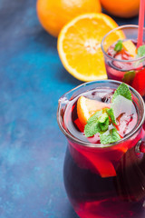 Refreshing Non-Alcoholic Spanish Sangria from Variety of Fruits Orange Citrus Pomegranate Grapes Berries and Fresh Mint in Pitcher and Tall Glass on Blue Background. Summer Vitamins Detox