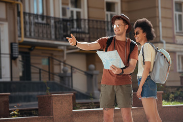 young male traveler with map pointing to african american girlfriend