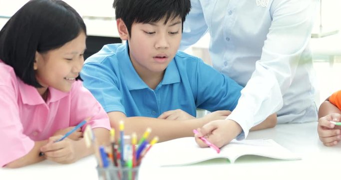 Young asian teacher helps young school kids in class, close up