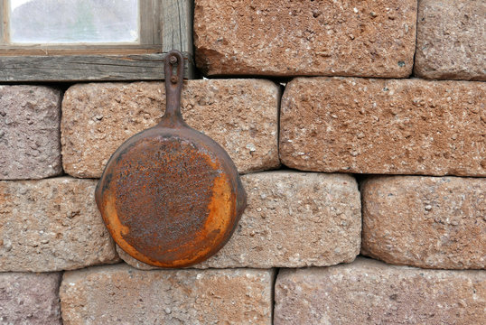 Old rusty frying pan hanging on an adobe wall