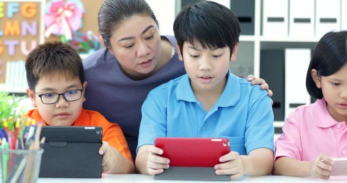 Asian teacher and Three kids entertaining themselves using digital tab and laughing