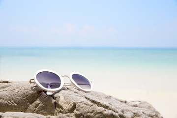 Sunglasses on tropical beach rock of blue sea in summer