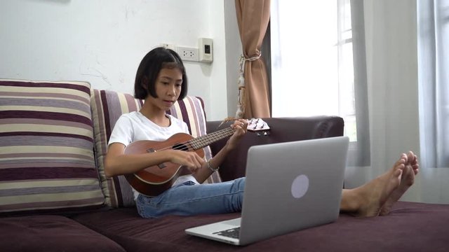 Little child playing ukulele with looking laptop computer at home