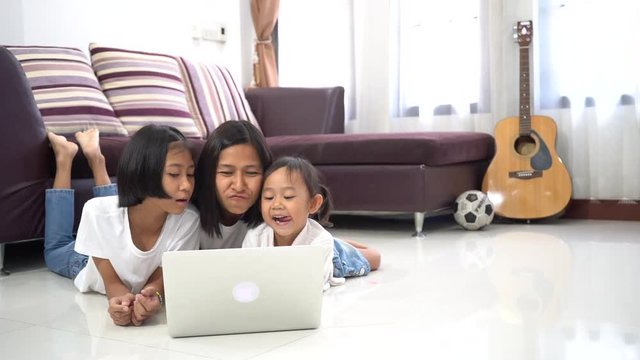 Happy mother and little daughter are lying on a floor at home and using a laptop computer, Slow motion