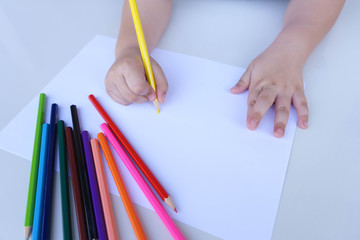 The child's hand preparing to write on a white sheet of paper with colored pencils.  Education and children activities concept.