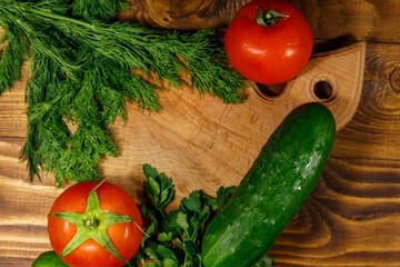 Fresh tomatoes, cucumbers, parsley and dill on cutting board on wooden table