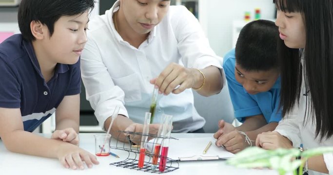 Teacher pouring chemical into test tube with his student in classroom .