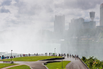 People walking in the fog on the observation deck next to Niagara Falls with the city on Background in USA