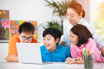 Teacher and Cute Asian children using laptop computer together.