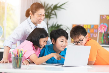 Teacher and Cute Asian children using laptop computer together.