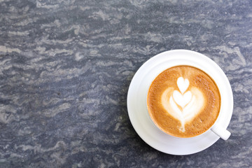 Cup of hot coffee with heart pattern in white cup on stone table background.