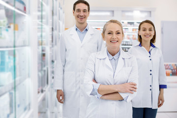 Come here. Enthusiastic three pharmacists smiling to camera while staying in drugstore
