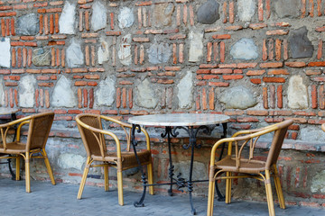 Tables and chairs in outdoor cafe. Patio set against stone wall
