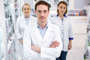 Fototapeta premium Work duty. Successful three pharmacists looking at camera while staying in drugstore