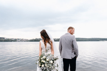 The bride and groom with a bouquet are happy together. An amazing couple on their wedding day are walking around the lake, hugging and enjoying each other.