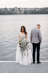 The bride and groom with a bouquet are happy together. An amazing couple on their wedding day are walking around the lake, hugging and enjoying each other.