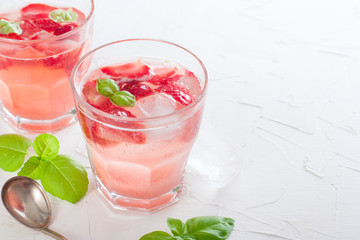 Fresh cool summer drink with strawberries and green basil in glass glasses on white table, horizontal, copy space