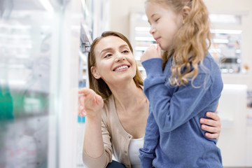 Mother and daughter. Jolly exuberant woman admiring girl who gazing at showcase