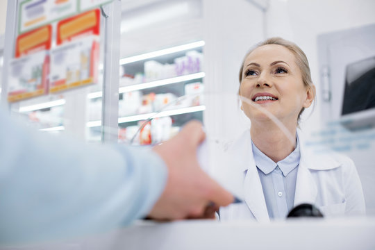 Your order. Low angle of happy female pharmacist smiling and talking with man