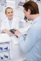 Obraz premium Enter password. Cheerful female pharmacist carrying terminal and man entering password